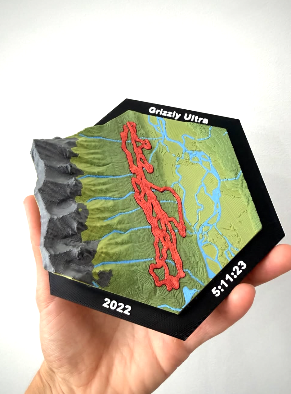 Hand holding a Grizzly Ultra 3D-printed topographic plaque with the race route in red